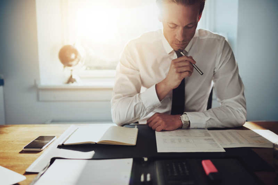 Serious business man working on documents looking concentrated with briefcase and phone on the table