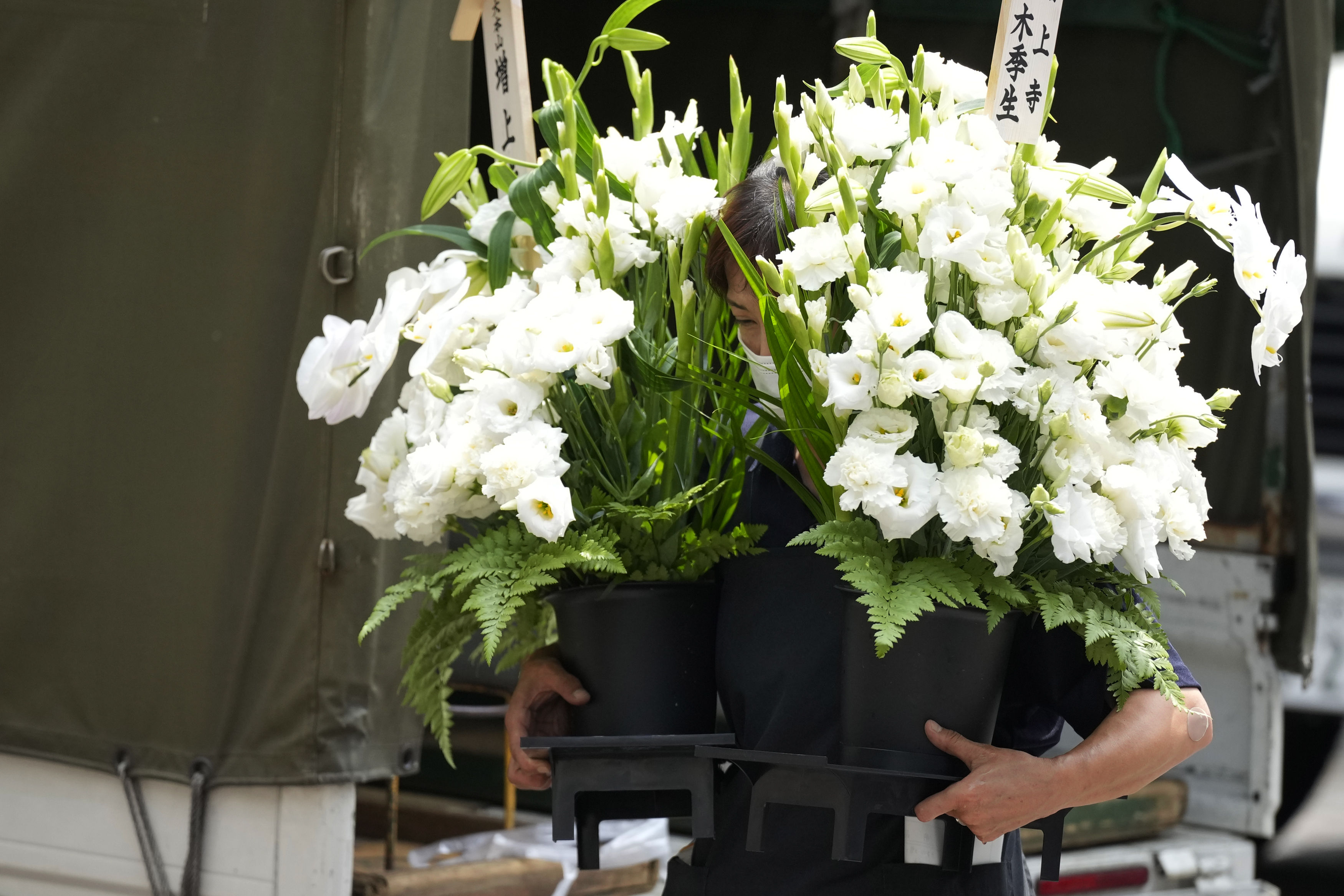 A worker brings a condolence flower to the residence of Japan's former Prime Minister Shinzo Abe who was assassinated Saturday, July 9, 2022, in Tokyo. The body of Japan’s former Prime Minister Shinzo Abe was returned to Tokyo on Saturday after he was fatally shot during a campaign speech in western Japan a day earlier.(AP Photo/Eugene Hoshiko)