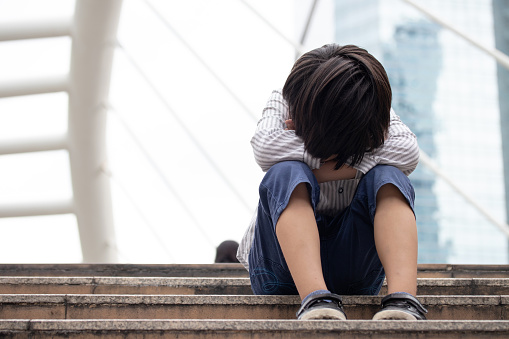 Homeless Asian child sitting alone on the stairway in the street. Poor, sad, scared and alone.