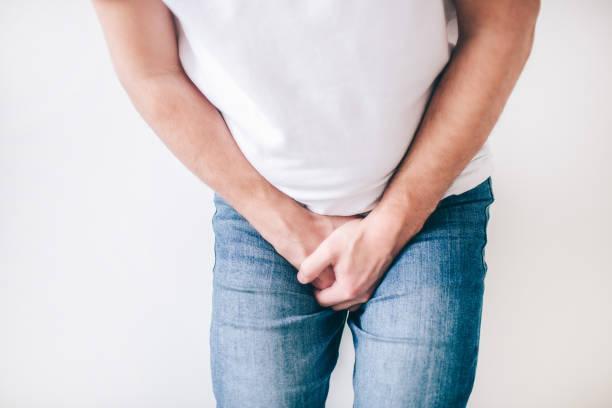 Young man isolated over white background. Cut view low part body. Guy hold both hands on crotch. Painful and terrible urine problem