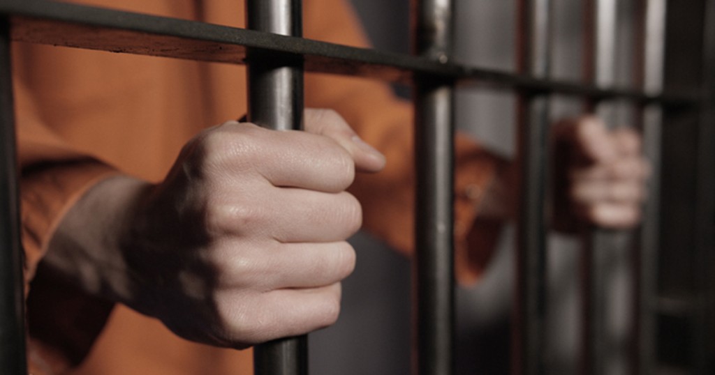 Man in Jail - Hands on Cell Bars of Prison