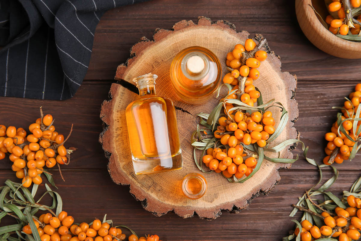 Natural sea buckthorn oil and fresh berries on wooden table, flat lay