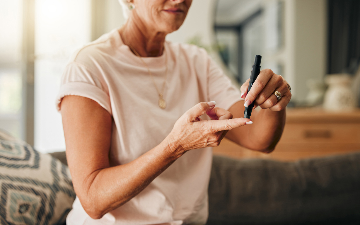 Diabetes, health and elderly woman doing a blood sugar test on her finger with a glucometer. Sickness, healthcare and diabetic senior lady checking her glucose level sitting on a sofa at home.