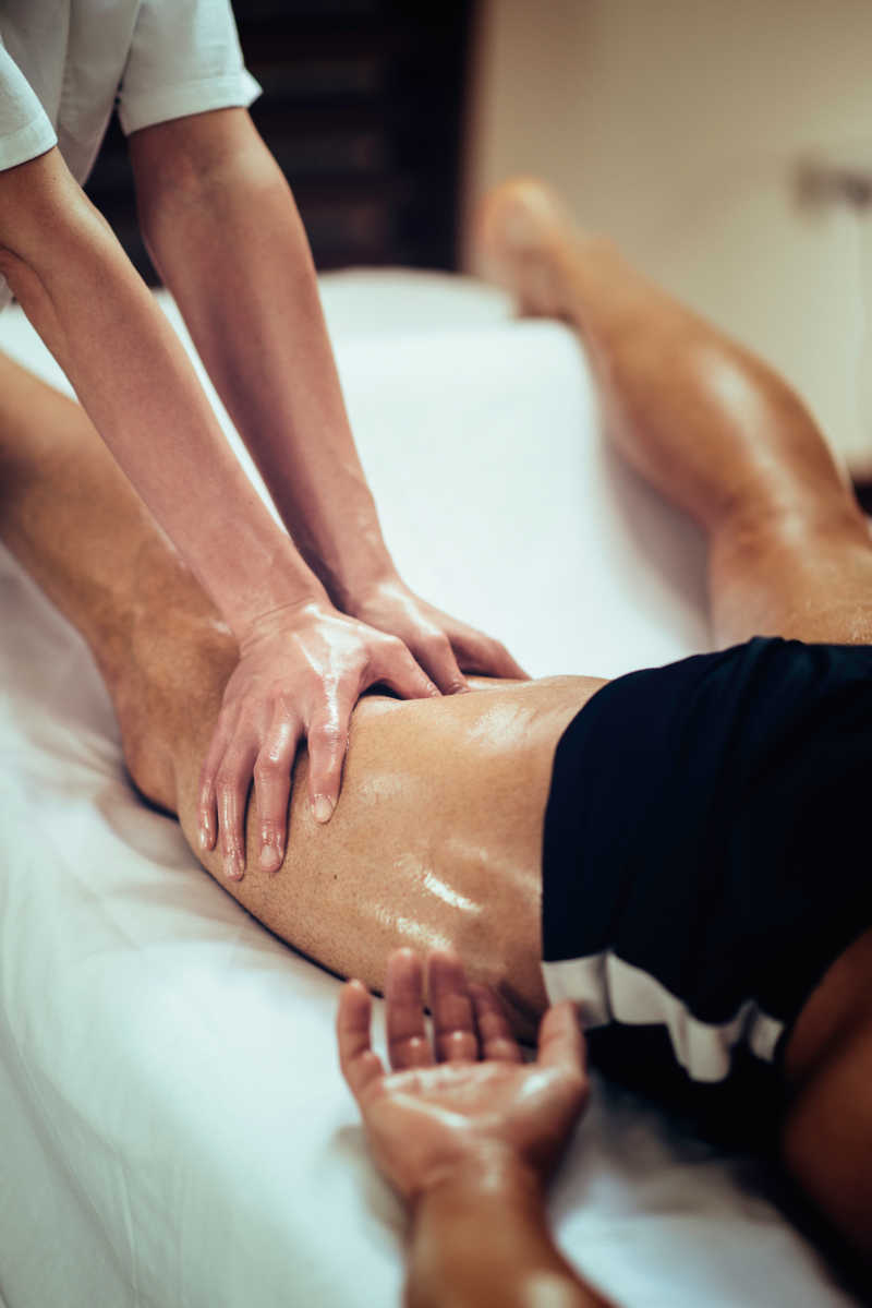 Female physical therapyst massaging leg of male athelete