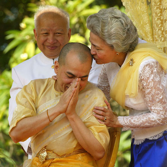 Cambodia's new King Nor在西哈努克和莫尼列见证下，儿子西哈莫尼继位成为柬埔寨国王。odom Sihamoni (C) is kissed by his mother Queen Norodom Monineath (R) while his father, former King Norodom Sihanouk looks on during a religious ceremony at the Royal Palace in Phnom Penh, 29 October 2004.  Traditional religious rituals for the coronation of new Cambodian monarch continues for the second day as his ascension to the throne nears.   AFP PHOTO / Jimin LAI