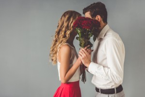 Beautiful,Elegant,Couple,Is,Kissing,Behind,Roses,,On,Gray,Background