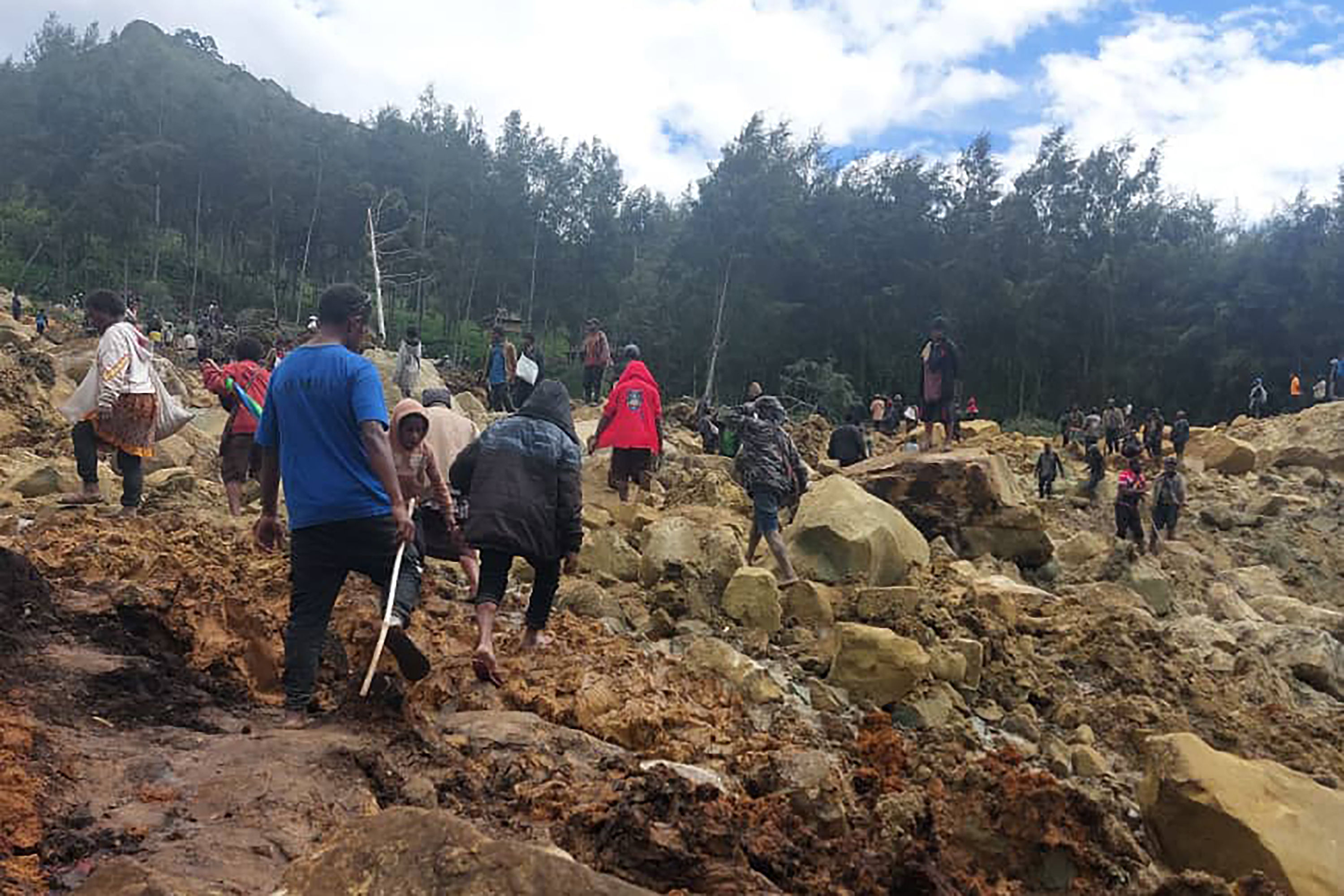 In this photo provided by the International Organization for Migration, people cross over the landslide area to get to the other side in Yambali village, Papua New Guinea, Friday, May 24, 2024. More than 100 people are believed to have been killed in the landslide that buried a village and an emergency response is underway, officials in the South Pacific island nation said. The landslide struck Enga province, about 600 kilometers (370 miles) northwest of the capital, Port Moresby, at roughly 3 a.m., Australian Broadcasting Corp. reported. (Benjamin Sipa/International Organization for Migration via AP)