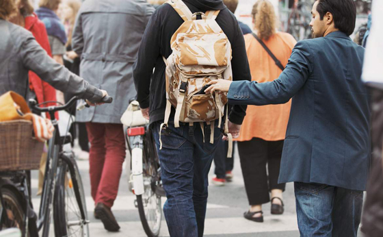 Young man taking wallet from backpack of a man walking on street during daytime. Pickpocketing on the street during daytime