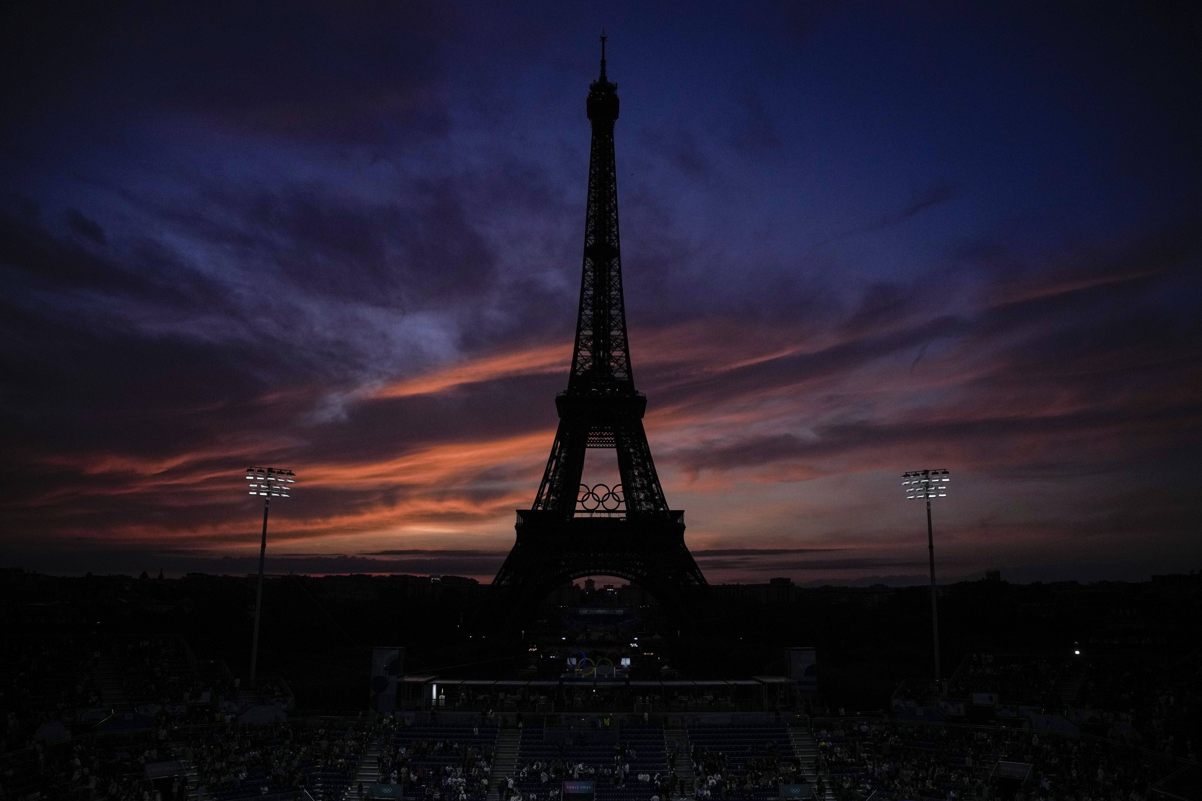 The Eiffel Tower is seen at sunset before the start of the women's pool B beach volleyball match between USA and Canada at Eiffel Tower Stadium at the 2024 Summer Olympics, Saturday, July 27, 2024, in Paris, France. (AP Photo/Louise Delmotte)