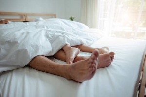 Love lying in bed in hotel,embracing on white sheets, close up legs.